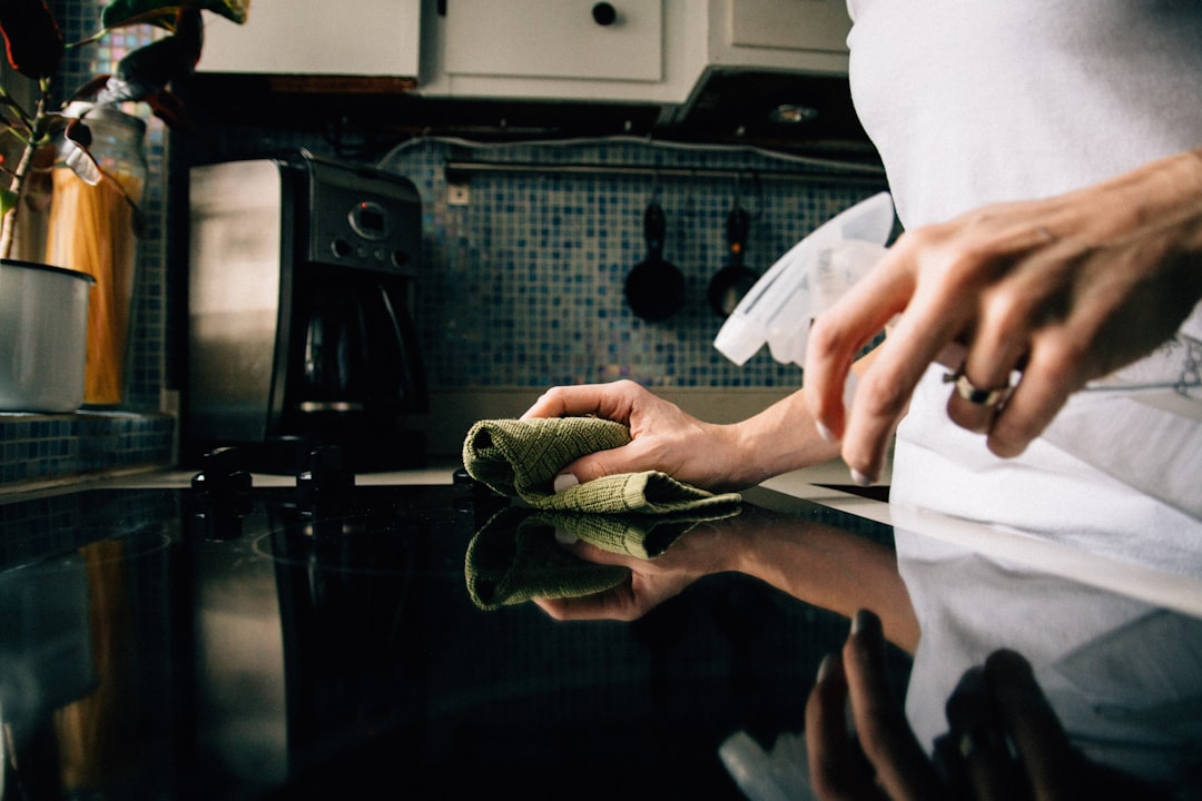 Hands wiping a glass stovetop after cooking as part of a clean-as-you-go kitchen routine