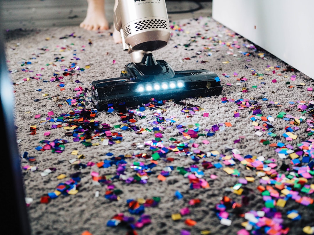 Person vacuuming a rug in a home, illustrating routine removal of dust, crumbs, hair, and debris from odor-holding surfaces