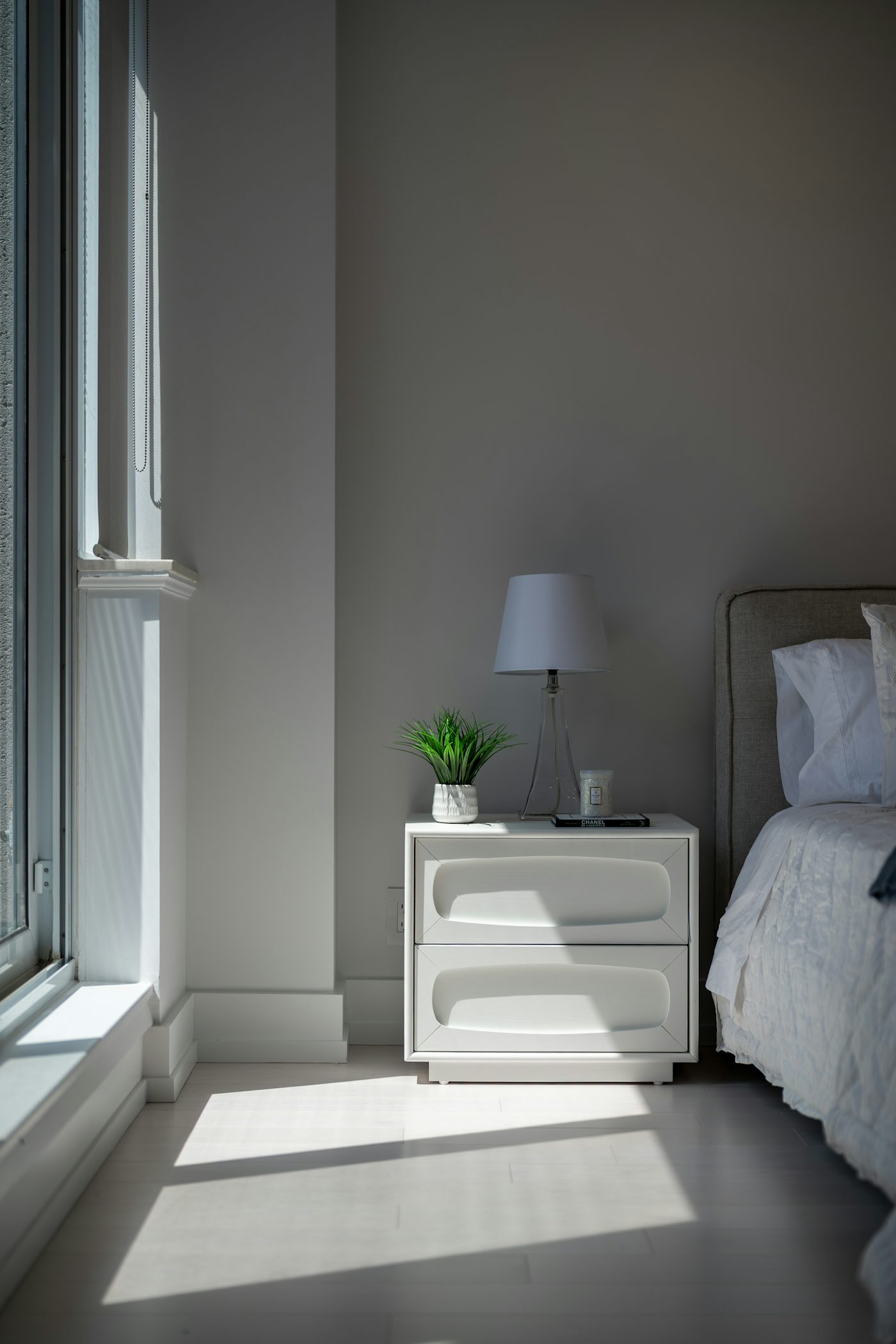 Sunlit bedroom featuring a white nightstand, lamp, and green plant