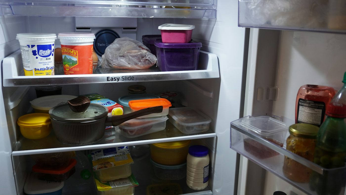 An open refrigerator filled with various food containers, jars, and a saucepan