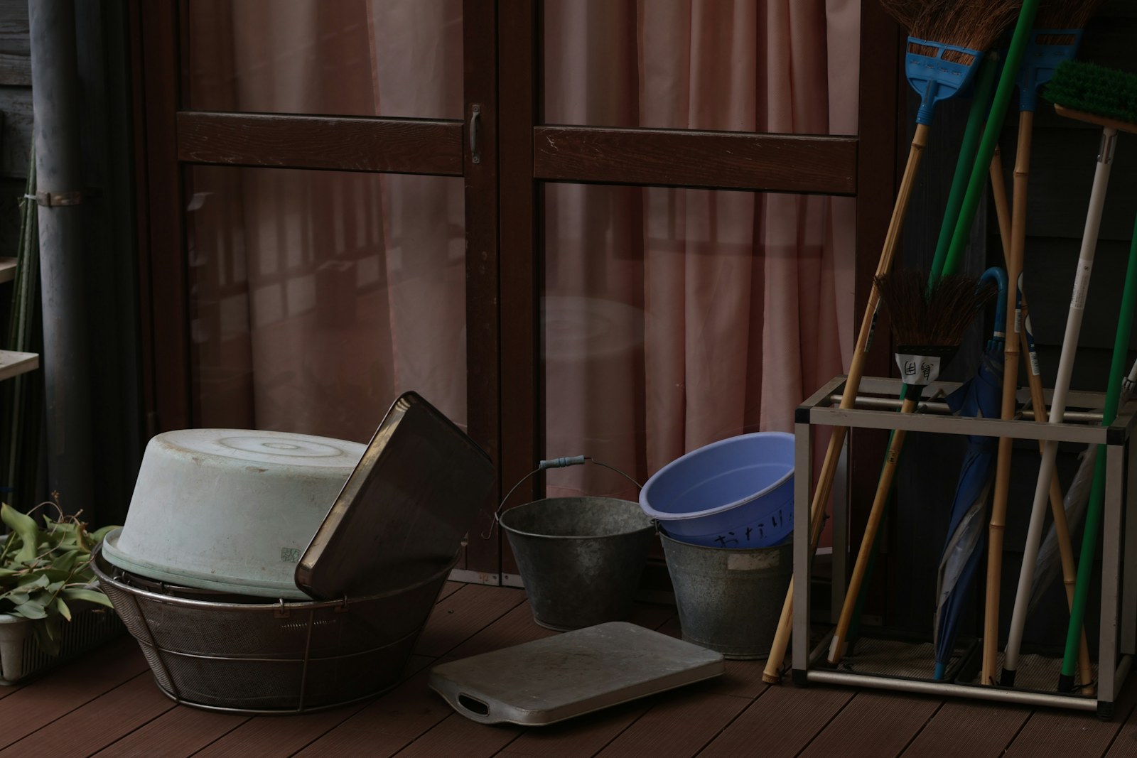 Cleaning supplies including buckets, a metal basket, and brooms on a wooden deck