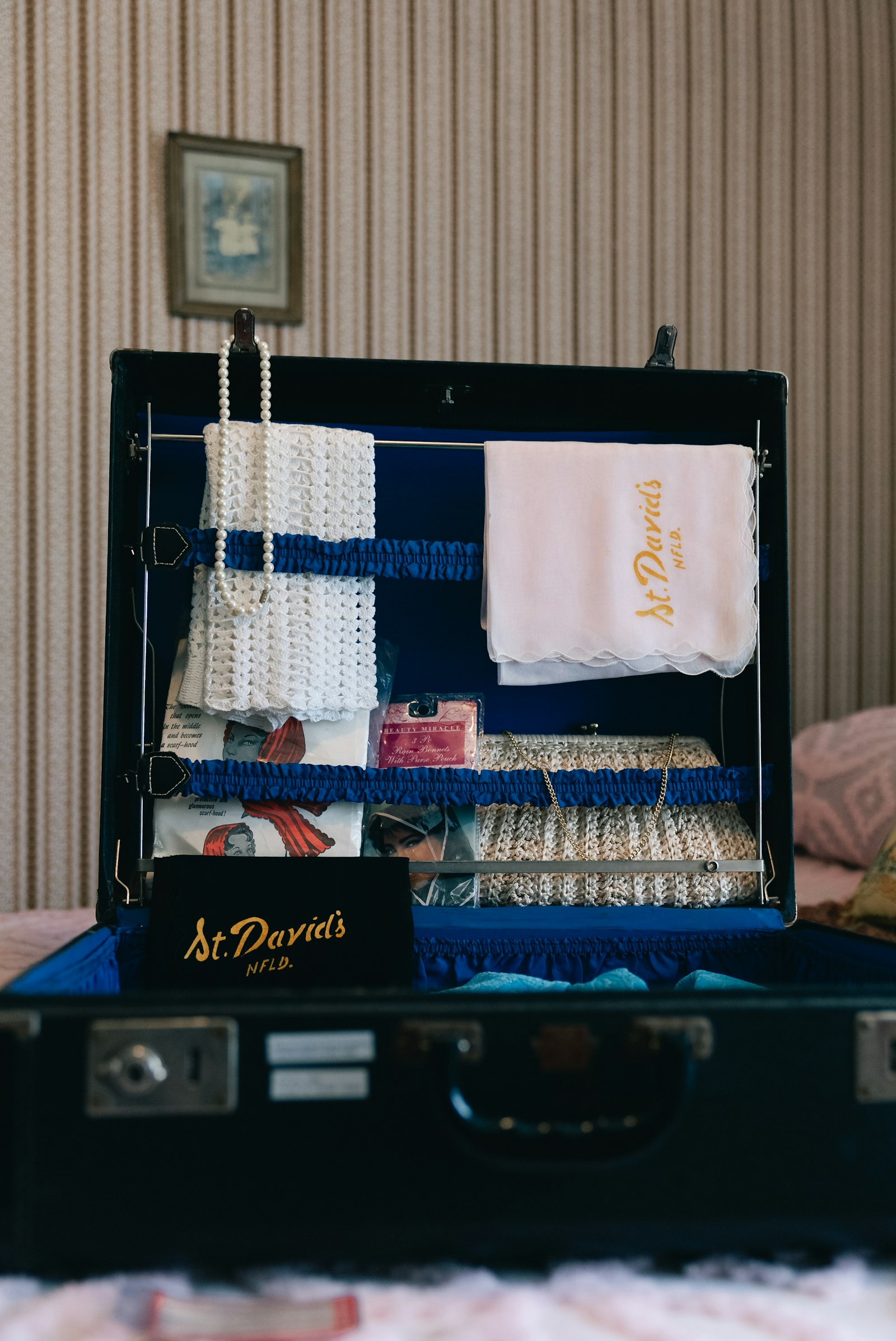 Vintage suitcase packed with pearl necklace, towel, and pink camera