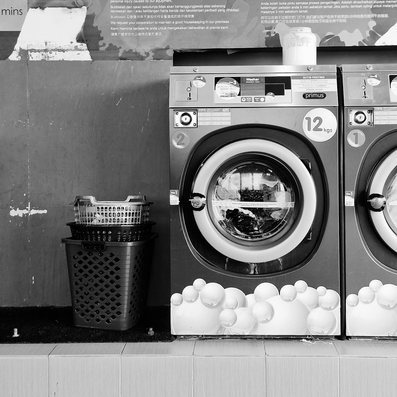 A black and white view of a washing machine beside stacked laundry baskets