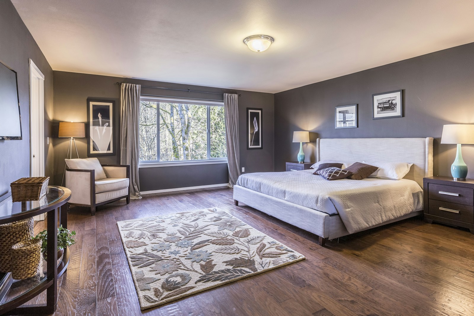 A bedroom with dark grey walls, a large bed, and a floral area rug