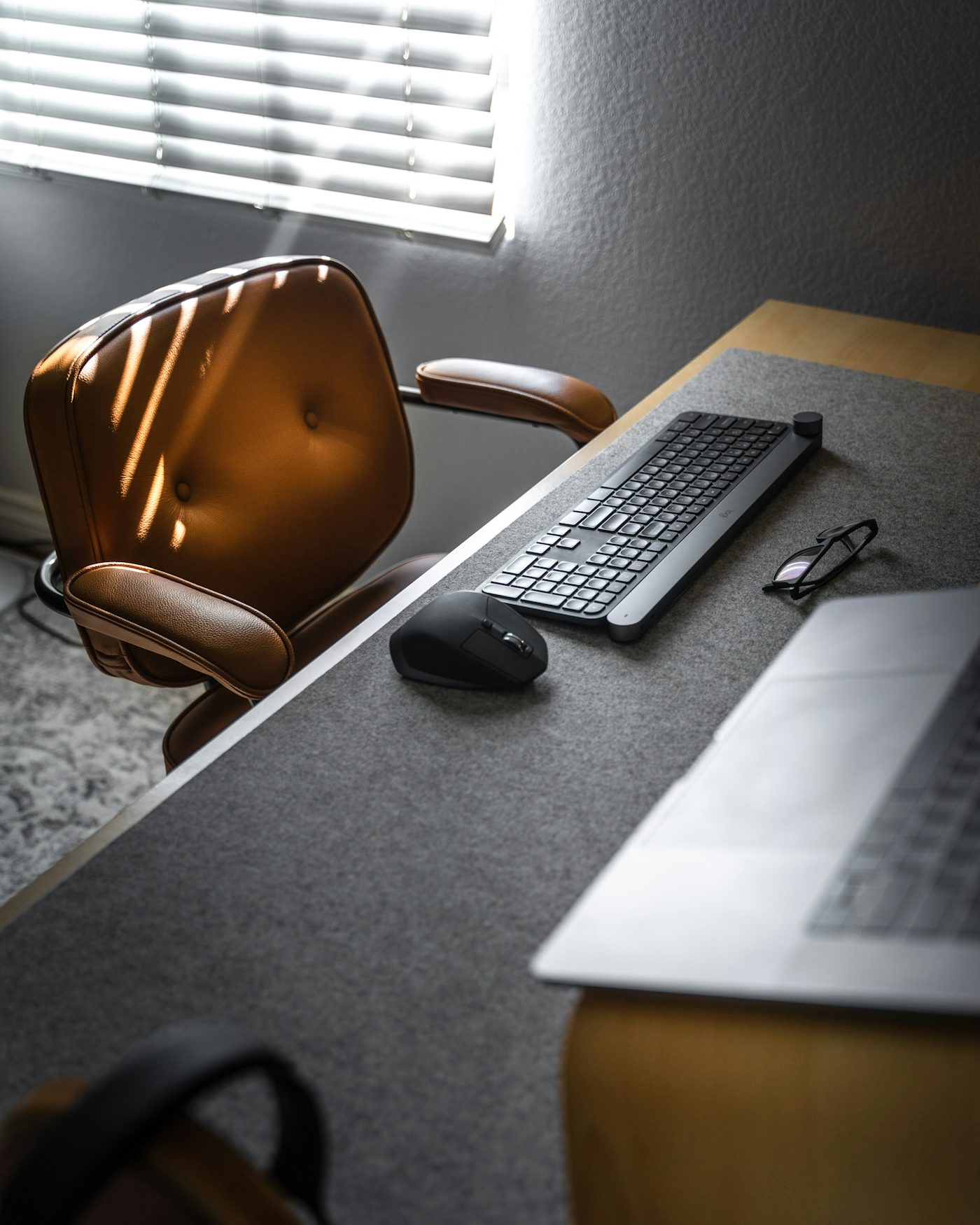 A brown leather office chair beside a desk with a keyboard, mouse, and laptop
