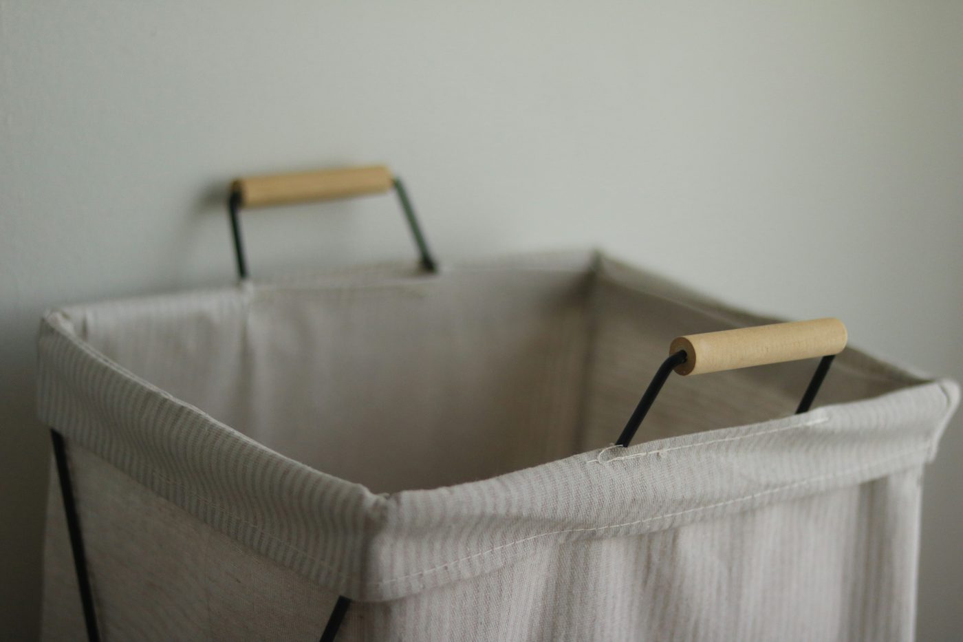 An empty, light-colored laundry hamper with wooden handles