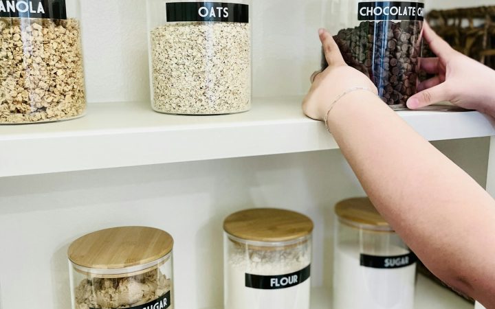 A person reaching for a glass jar of chocolate chips on a pantry shelf
