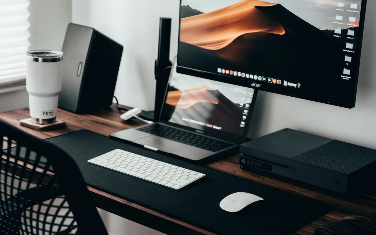 A home office workspace with a laptop, monitor, and keyboard on a wooden desk