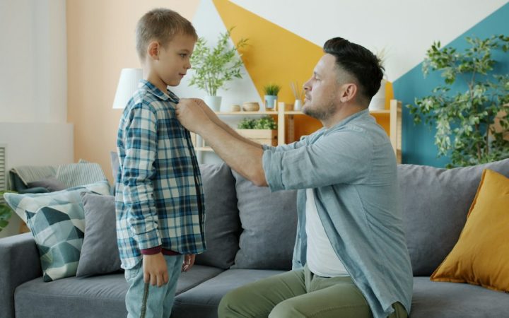 Parent helping a child prepare clothing during the morning