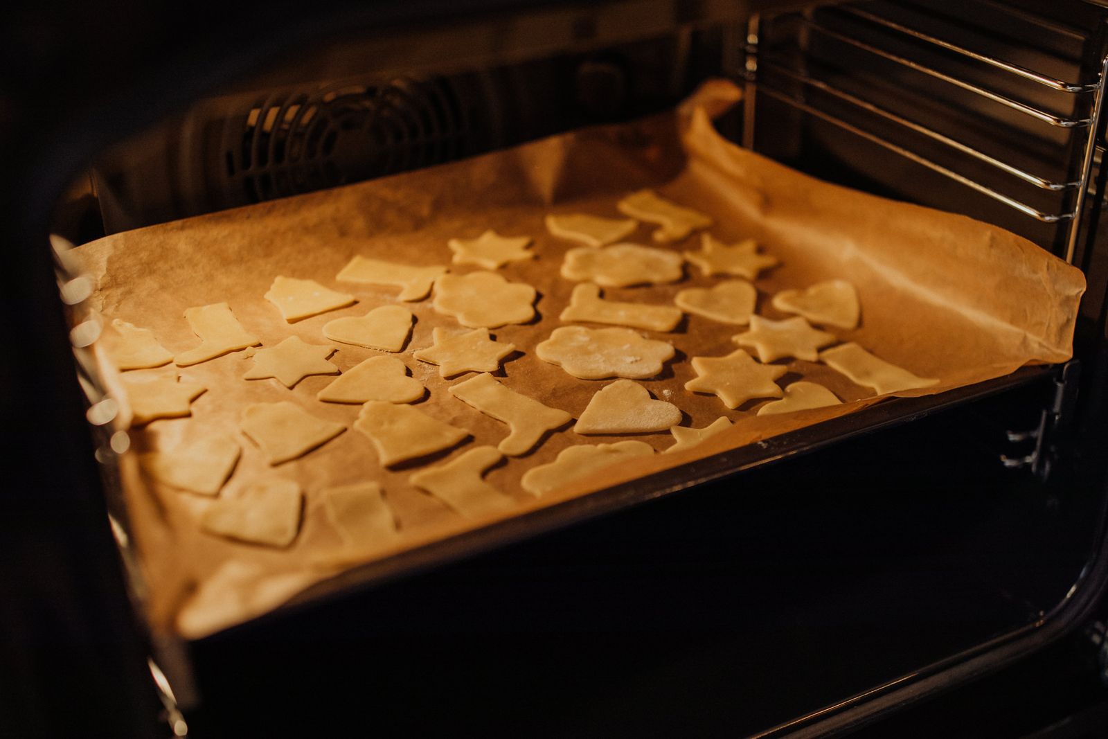 Shaped cookies on a parchment-lined sheet inside an oven