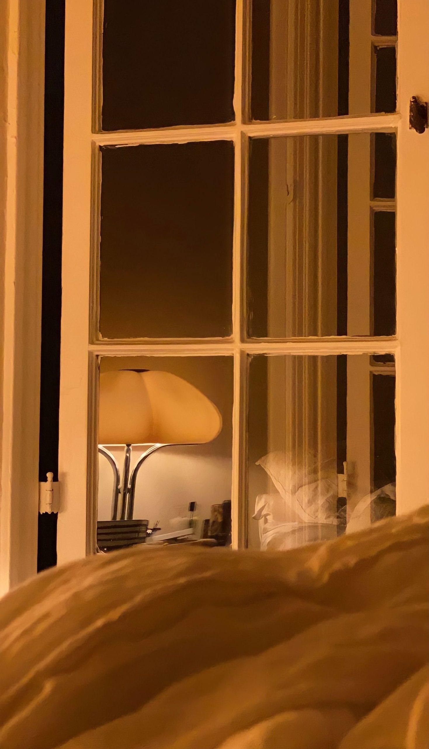 A bedroom and lit bedside lamp viewed through a window