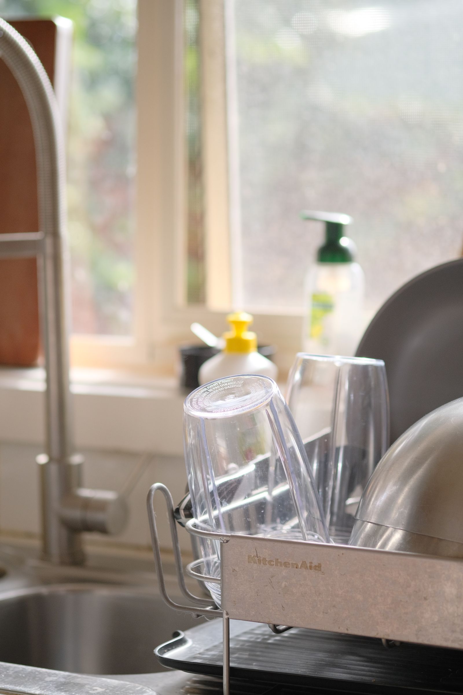 Clean glasses and dishes drying in a rack beside a kitchen sink