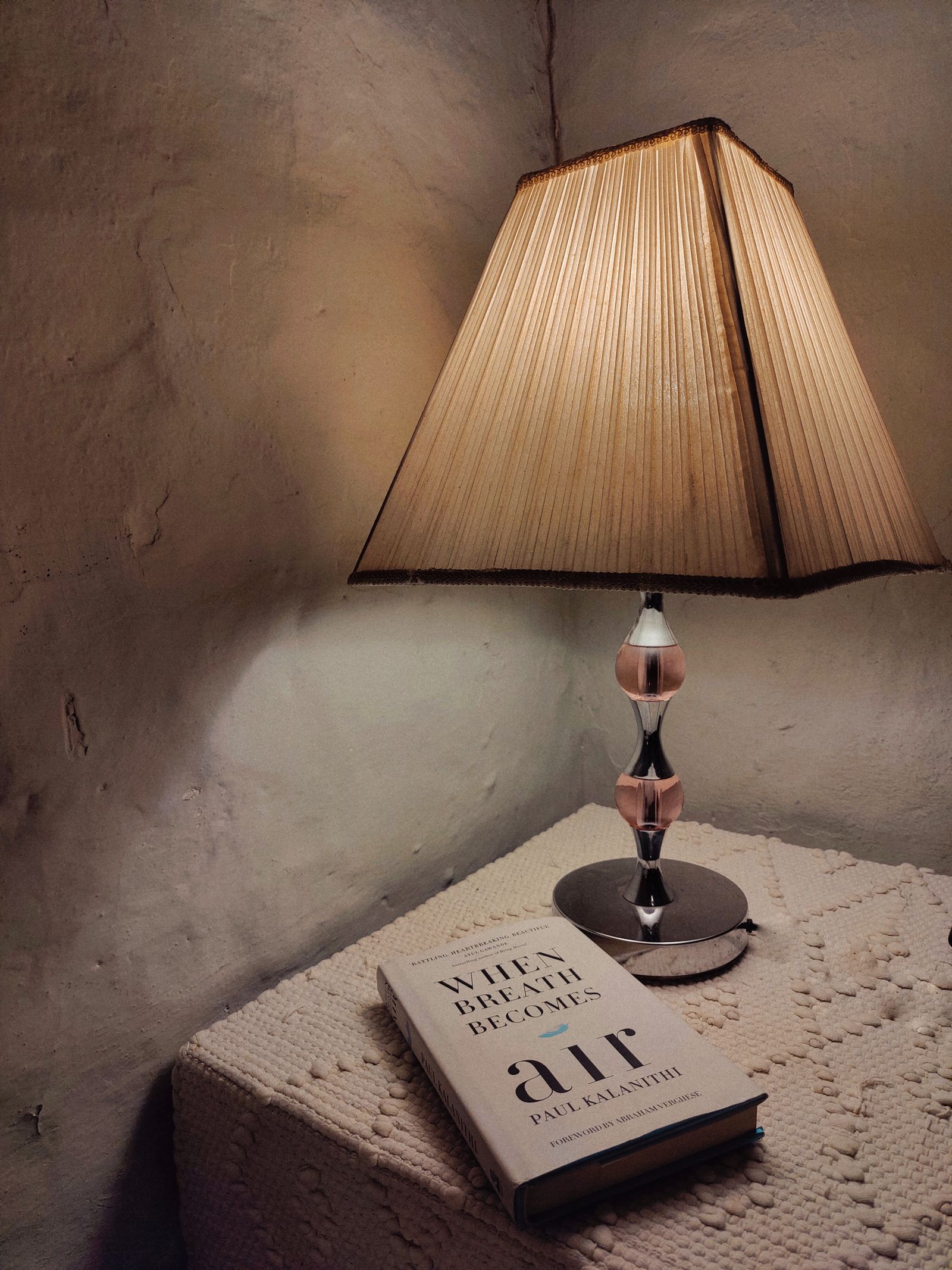 A pleated lampshade above a bedside table and book