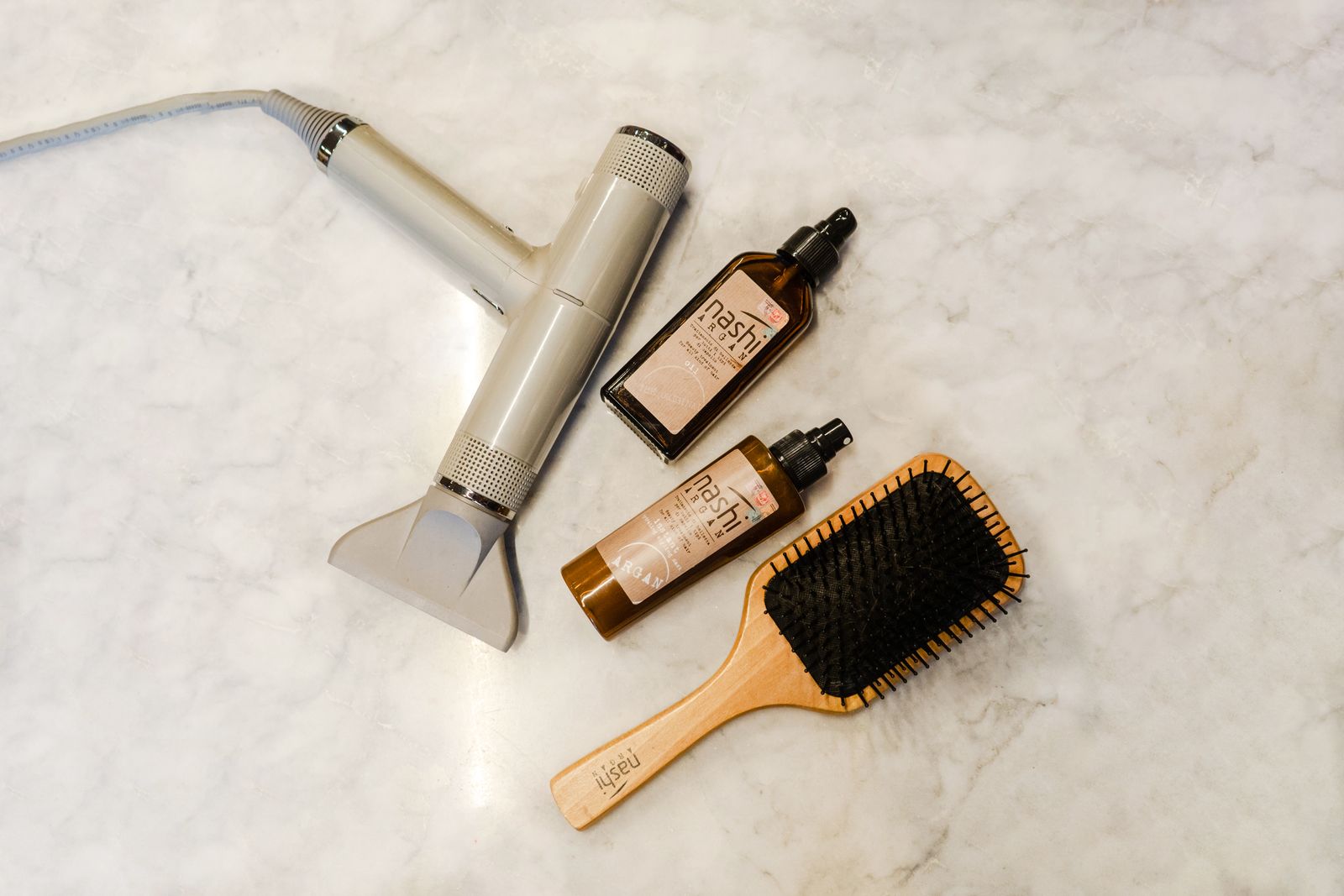 A hairdryer, hairbrush, and hair products laid out on a dry surface