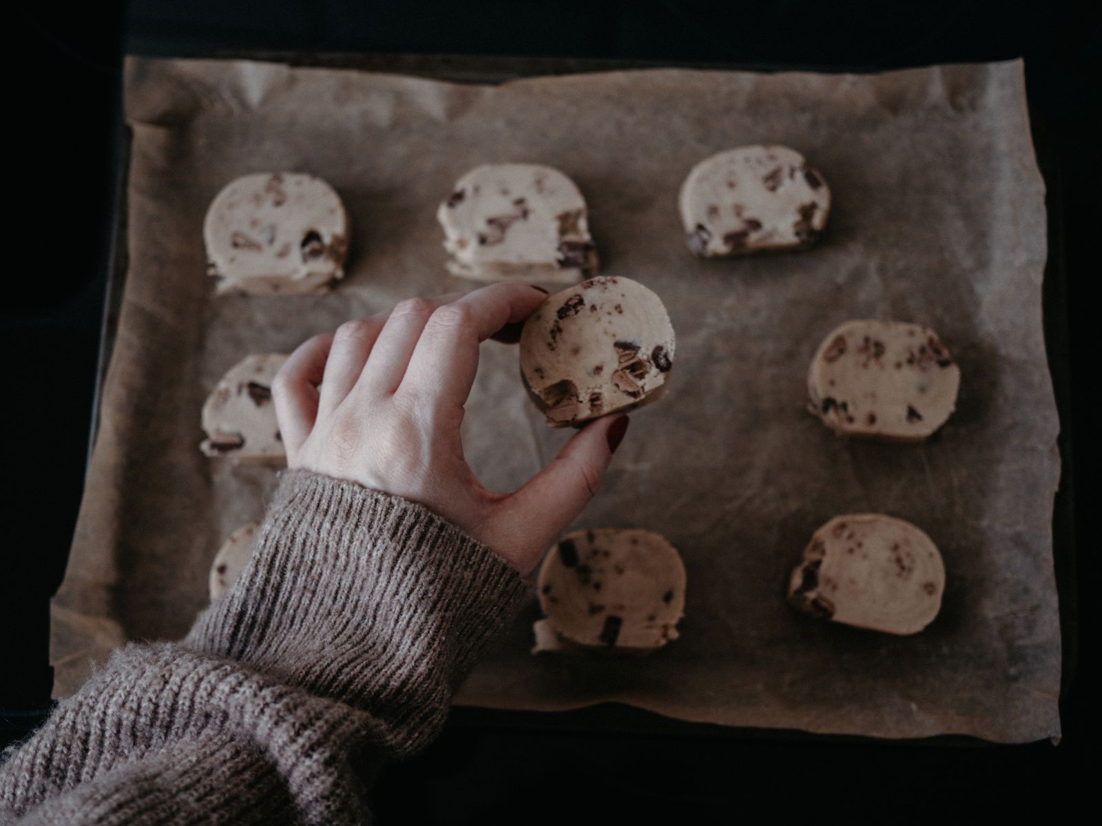 A hand arranging cookie dough on a parchment-lined baking sheet