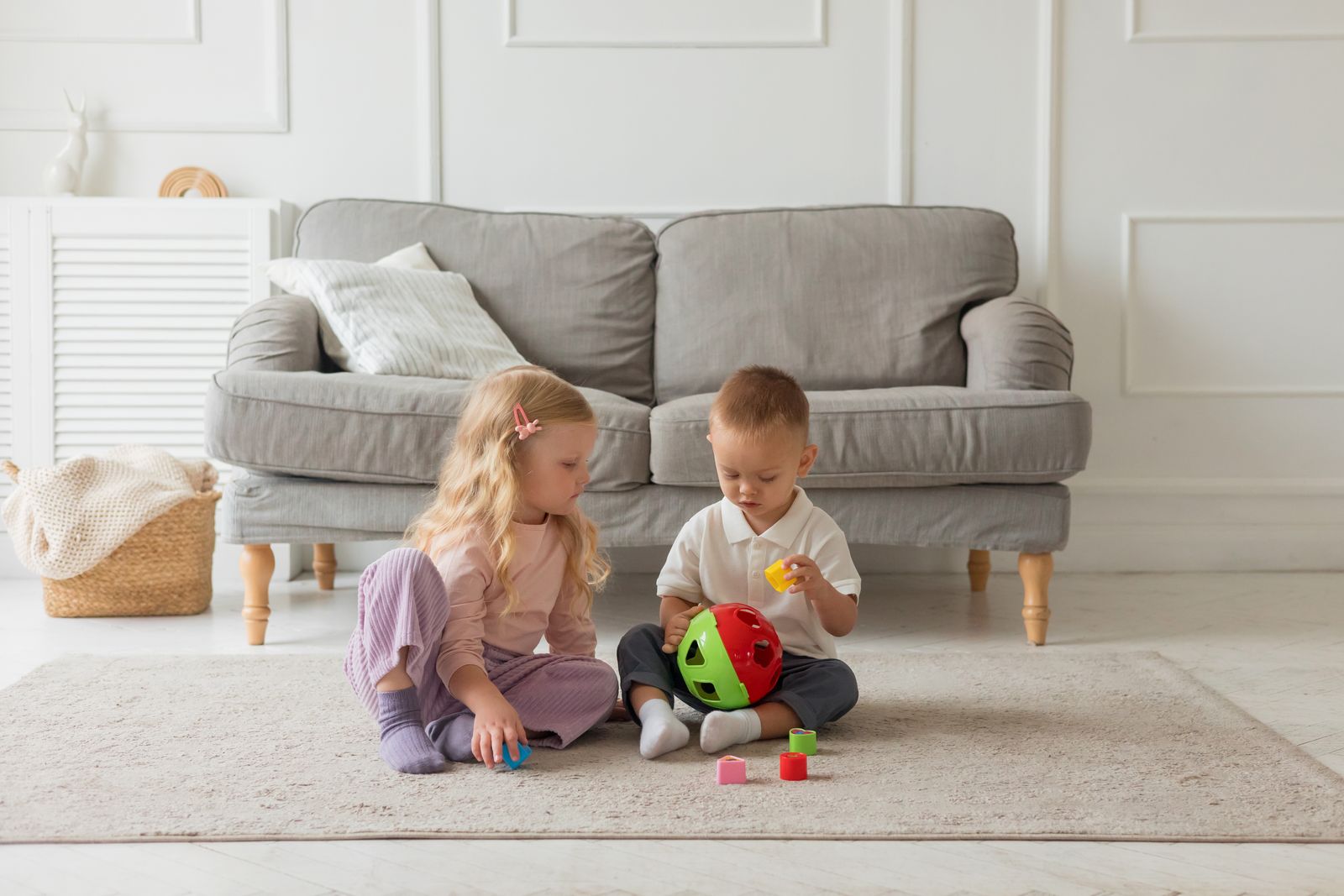 Two children sharing a colorful toy on a rug beside a sofa