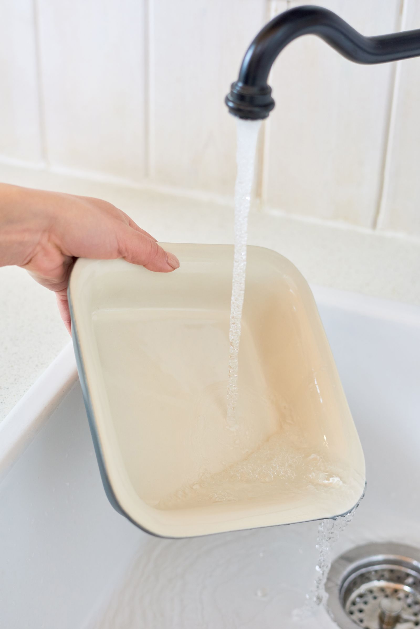A ceramic baking dish being rinsed under a kitchen tap