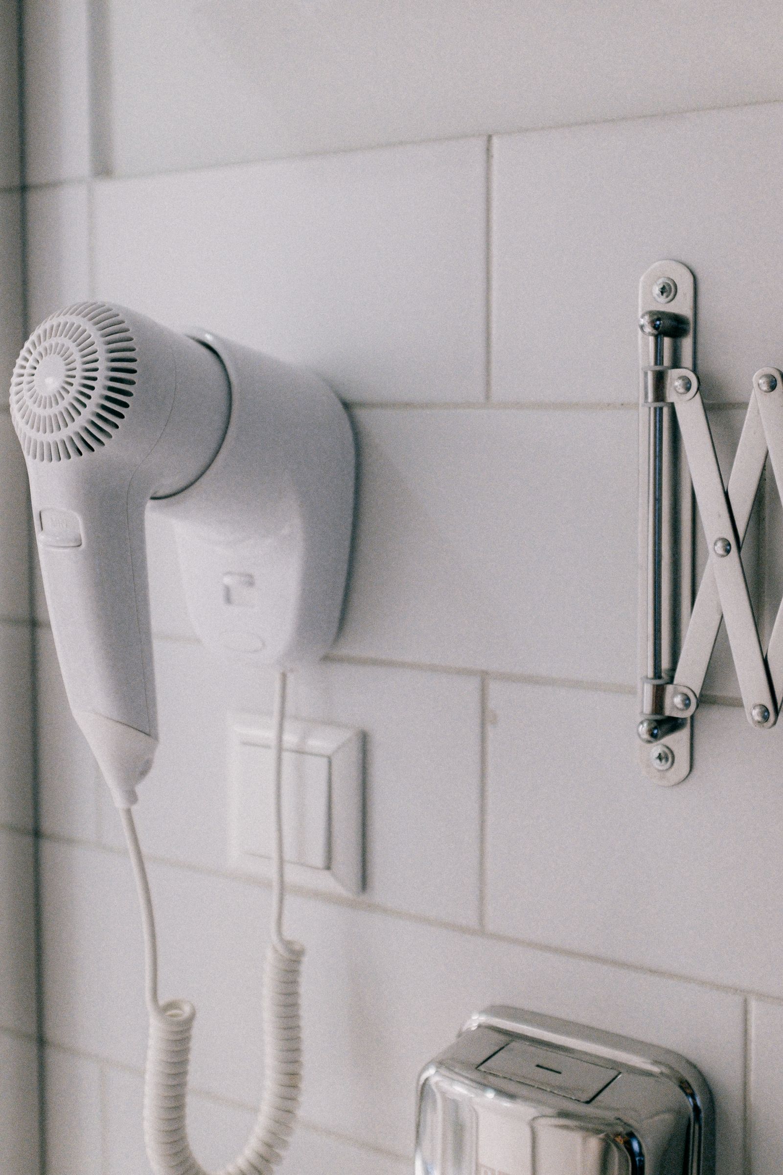 A wall-mounted hairdryer with its cord and holder