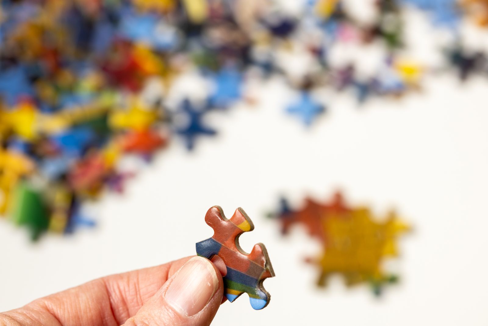 A hand holding a jigsaw piece above other pieces