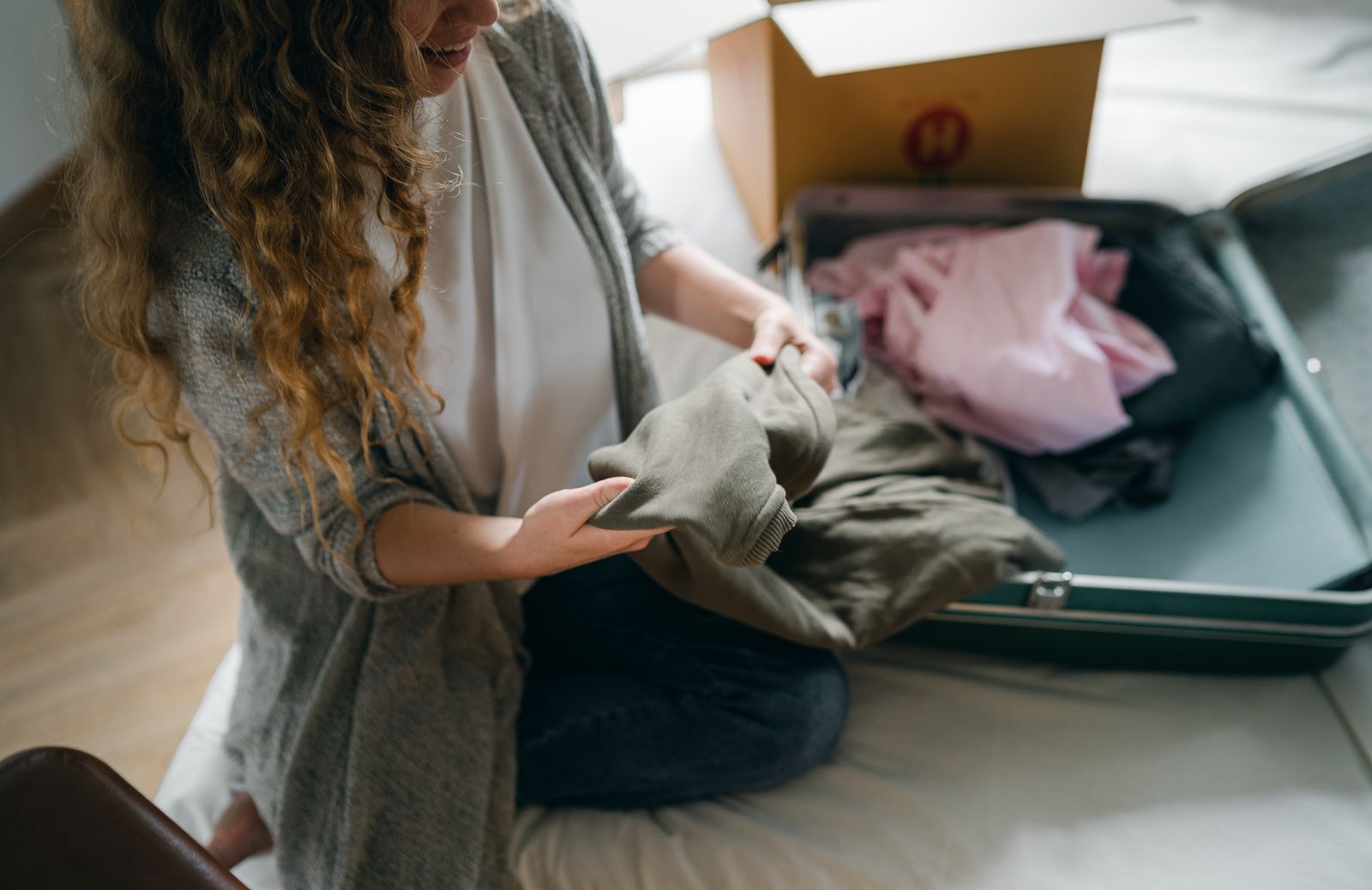 An adult folding clothing beside an open suitcase on a bed