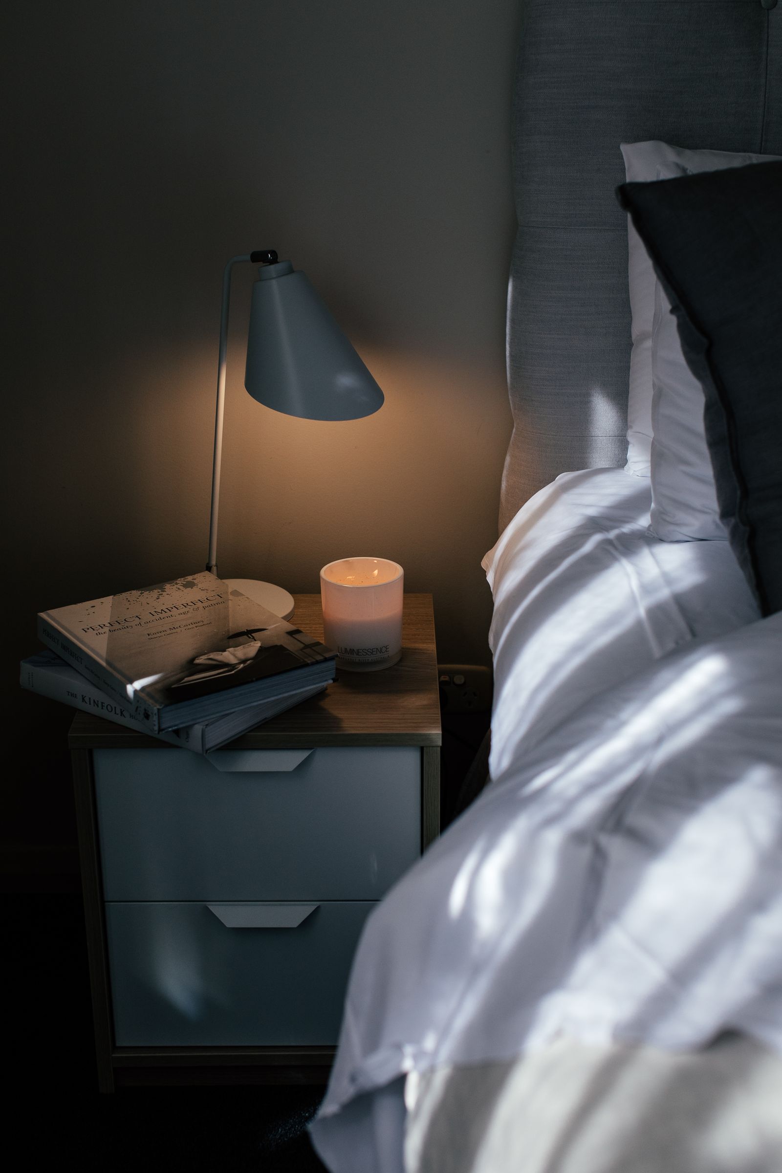 A bedside lamp and books beside a made bed