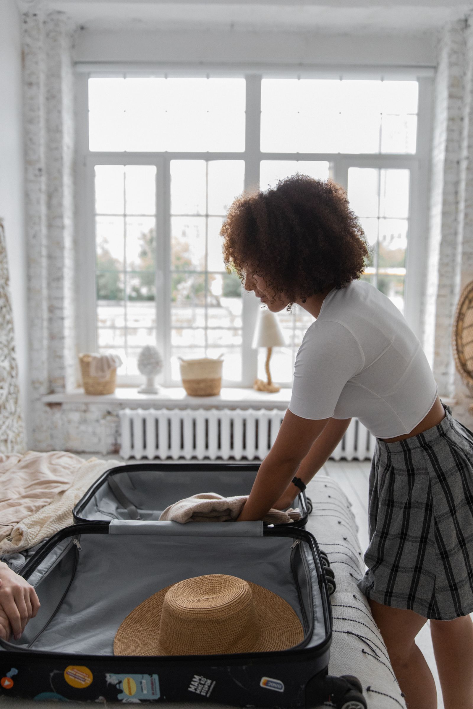 An adult arranging clothing in a suitcase in a bedroom