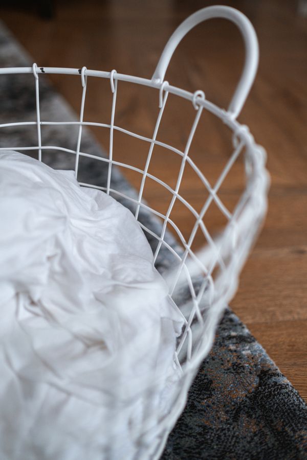 White wire laundry basket with clothes on a hardwood floor, showing a compact hamper footprint