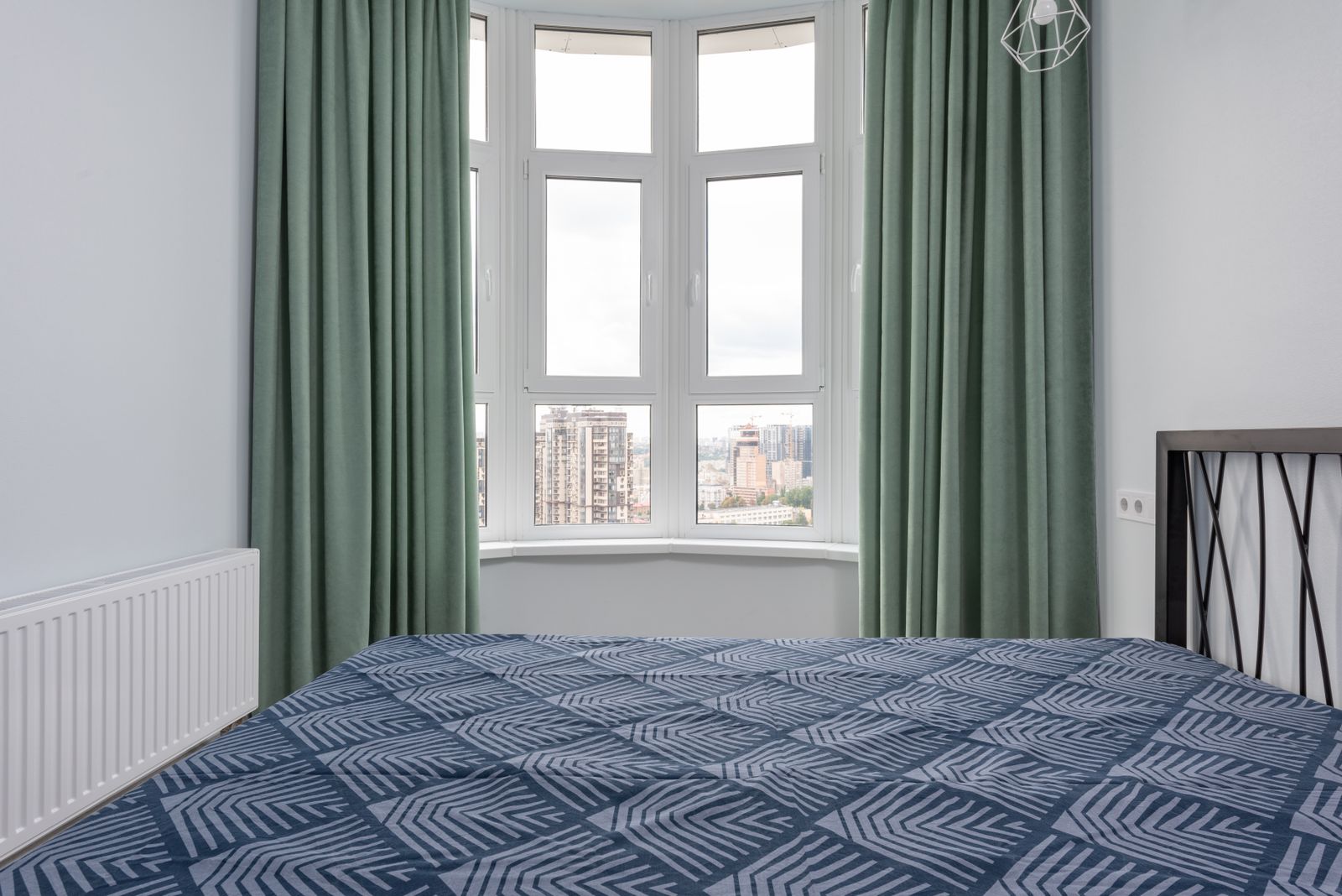 A bed positioned beside a window and wall radiator