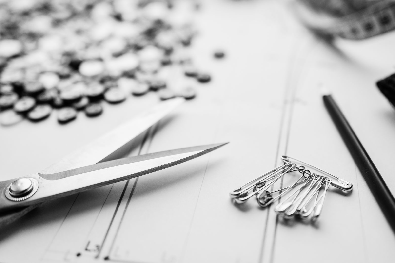 Scissors, pins, buttons, and a pencil on a light surface