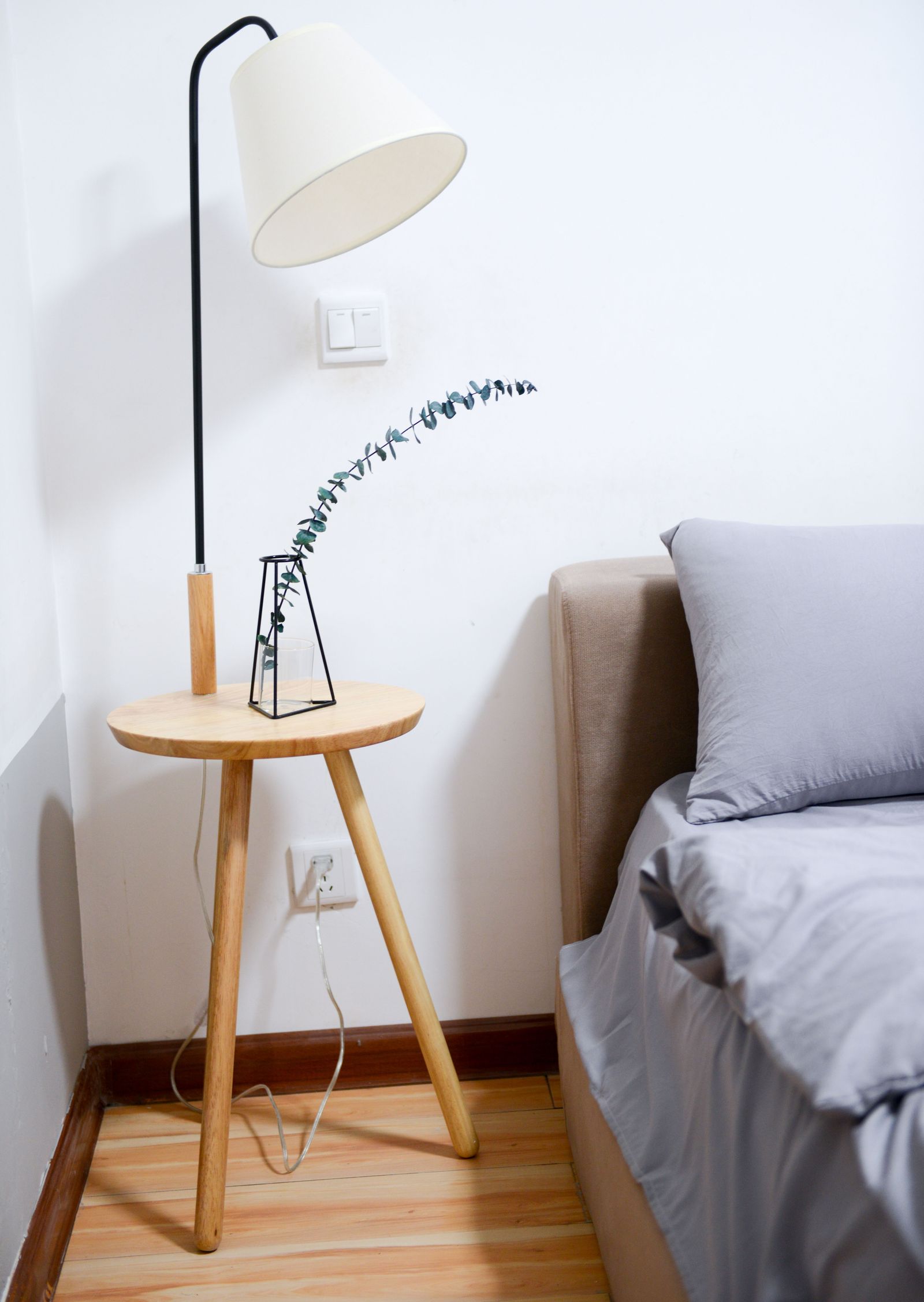 A metal-shade floor lamp beside a bed and small table