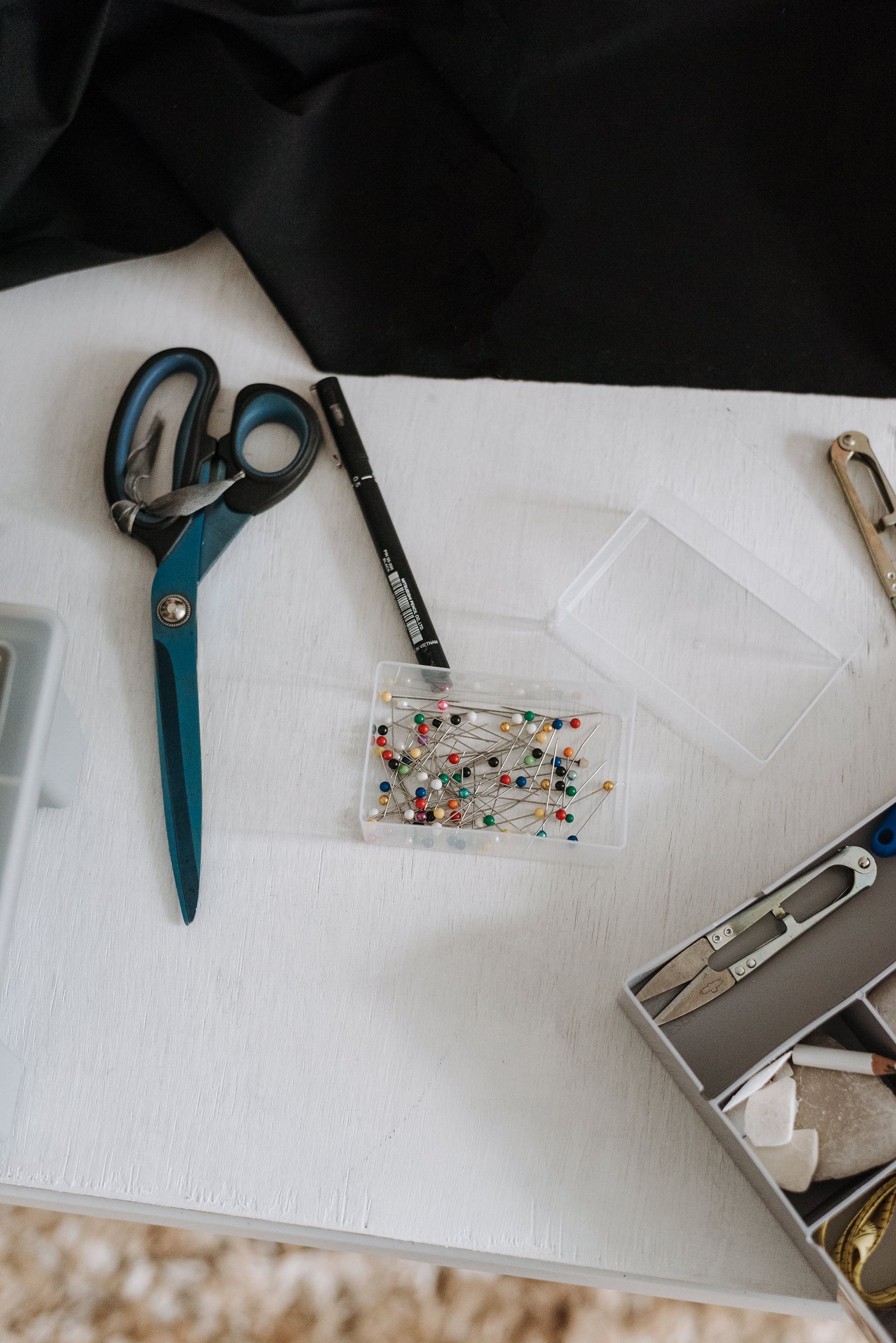 Scissors and sewing pins beside fabric on a work surface