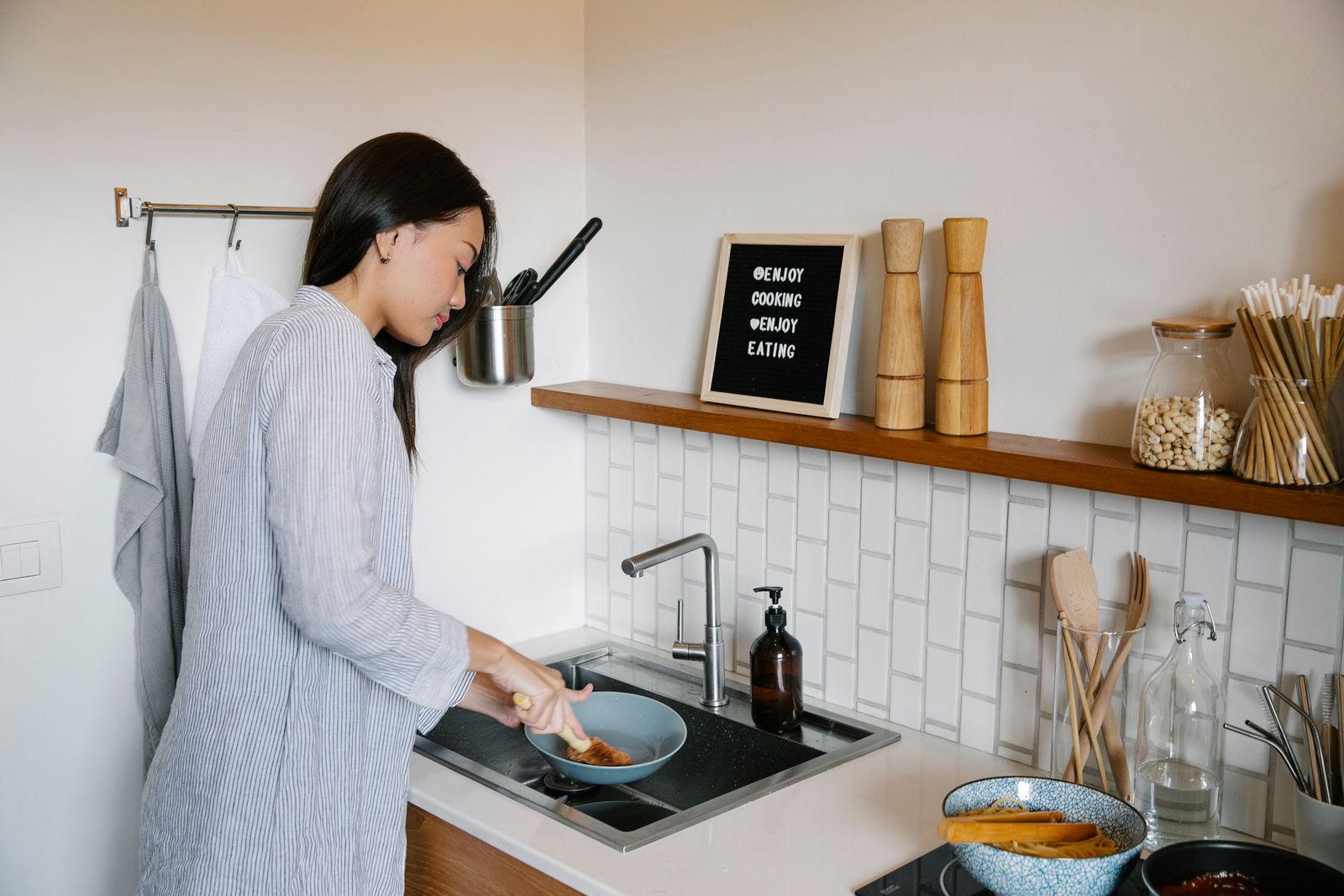 A woman washing a plate with a brush in a home kitchen
