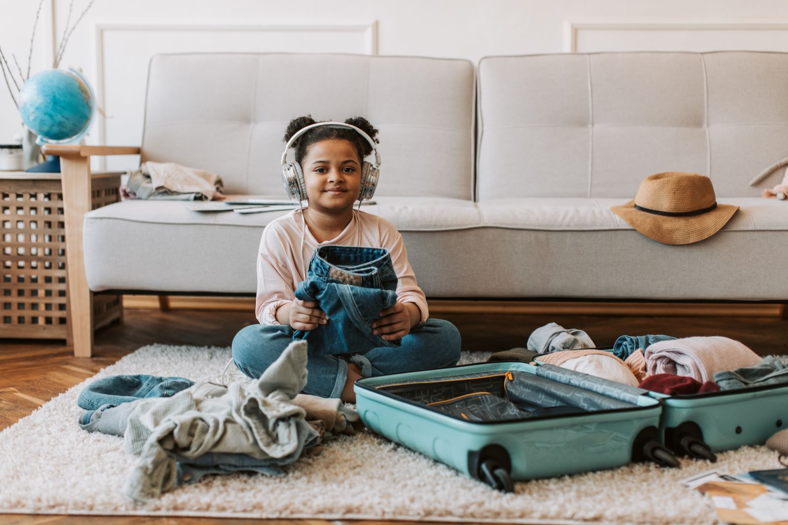 A child holding clothing beside a small open suitcase