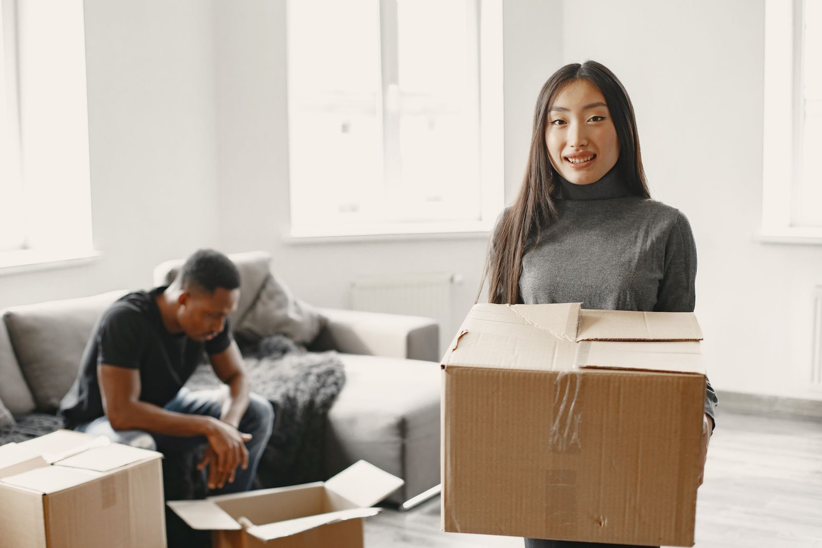 Two people with moving boxes beside a living-room sofa
