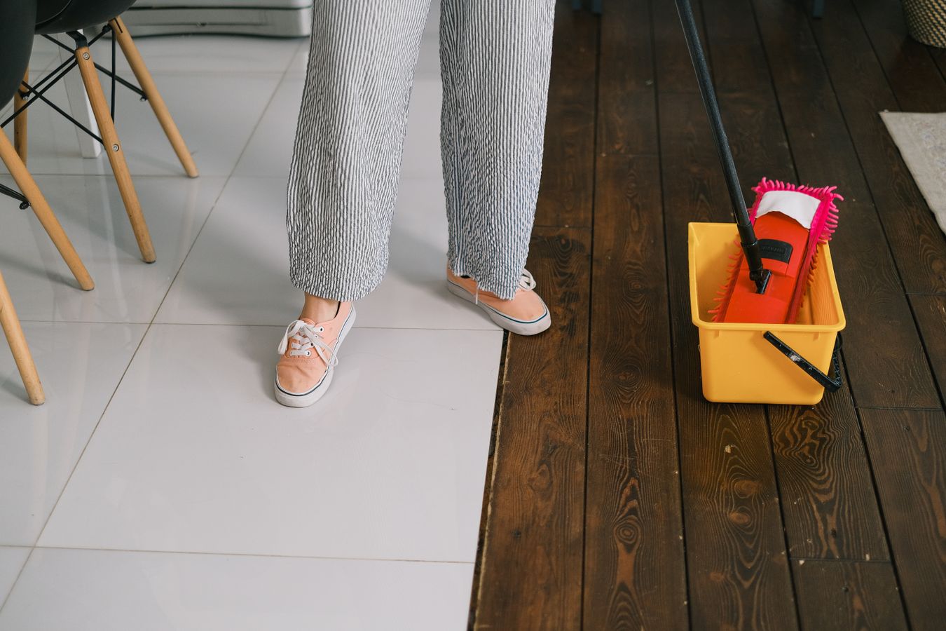 Person preparing a mop and bucket on a wooden floor for routine cleaning