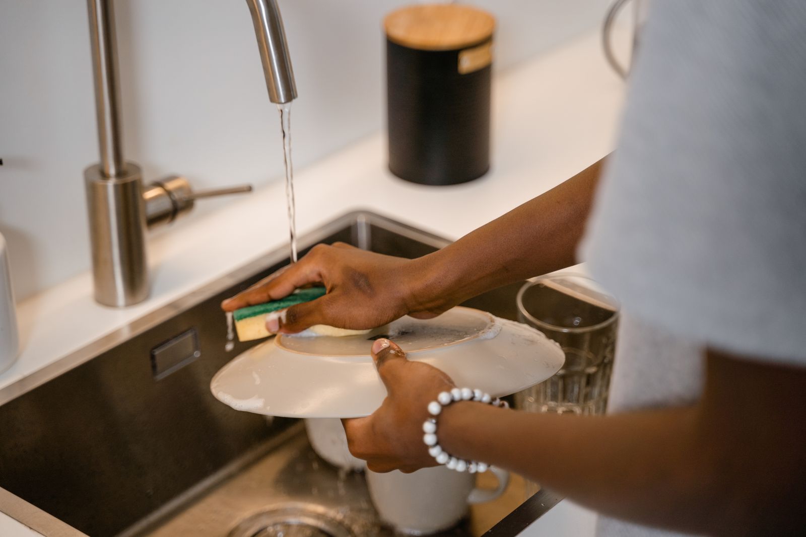 Hands washing a ceramic plate at a kitchen sink