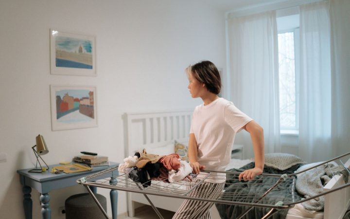 Woman in a small bedroom with clothes and a drying rack, illustrating everyday clothing clutter