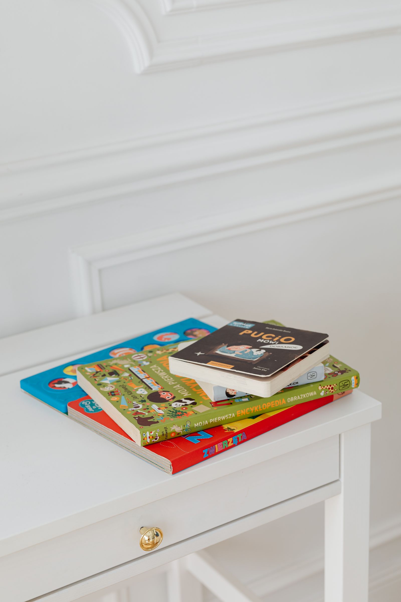 A small stack of picture books on a white bedside table