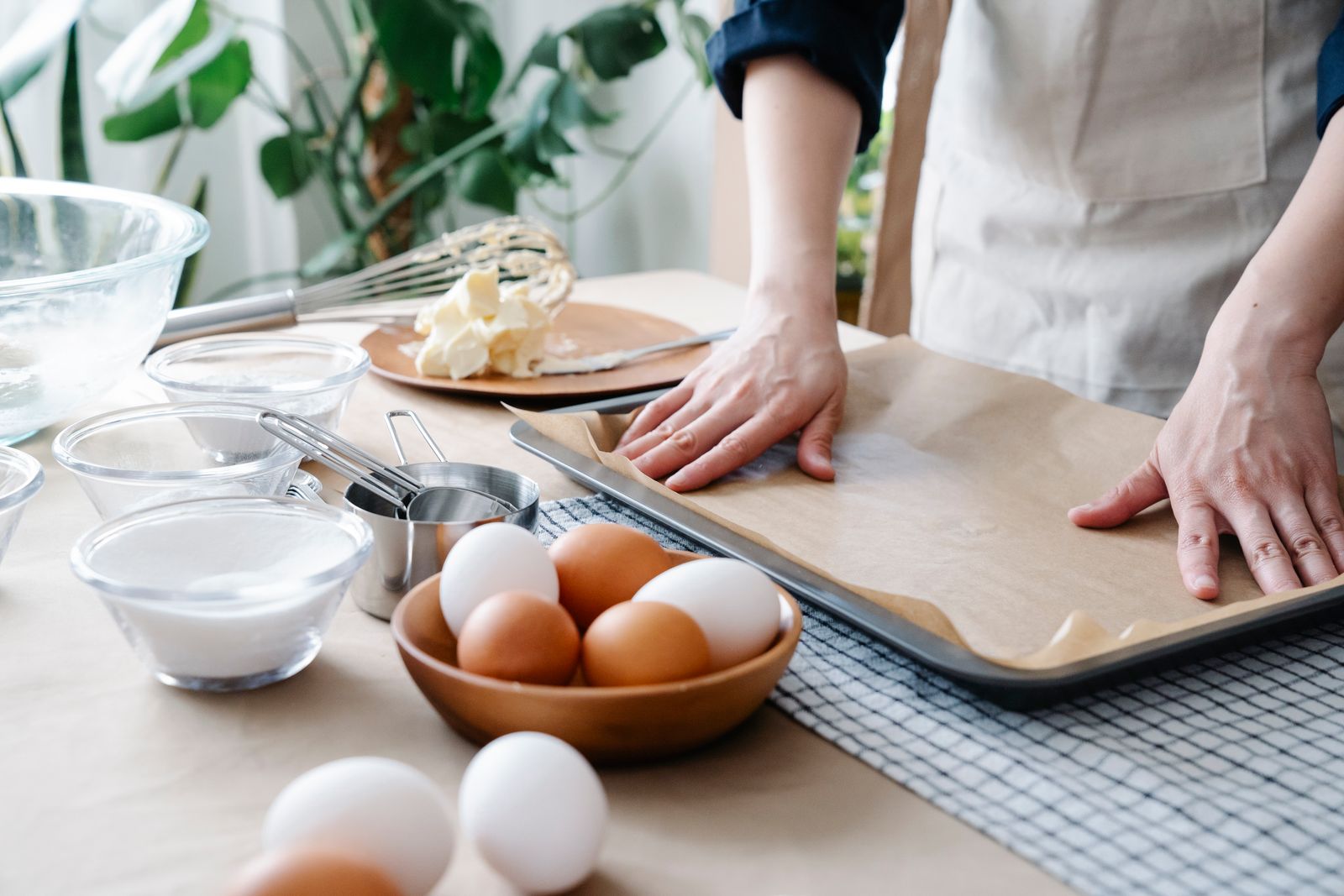 Hands rolling dough on parchment beside baking ingredients