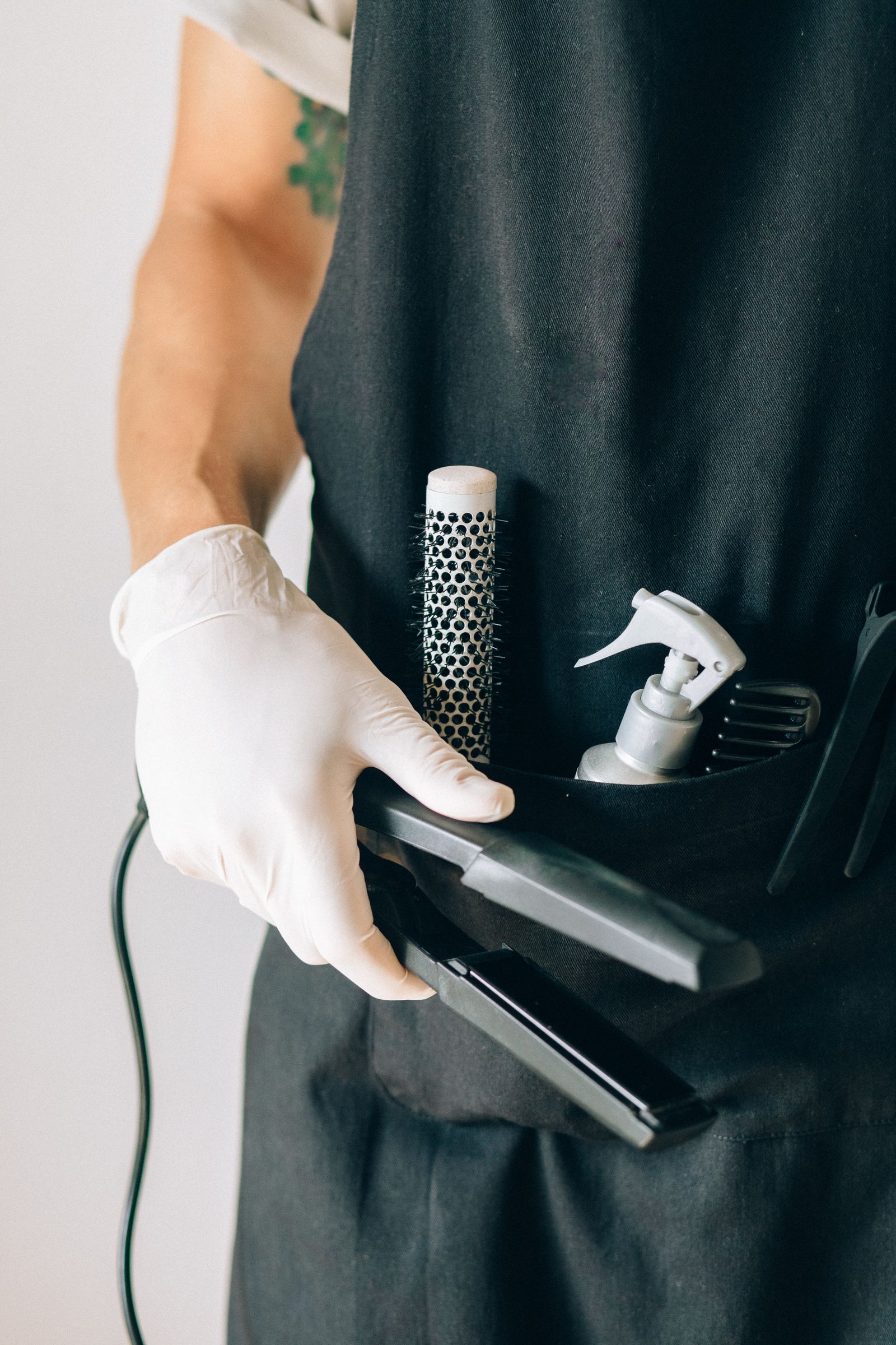 A stylist holding a straightener near an apron tool pocket