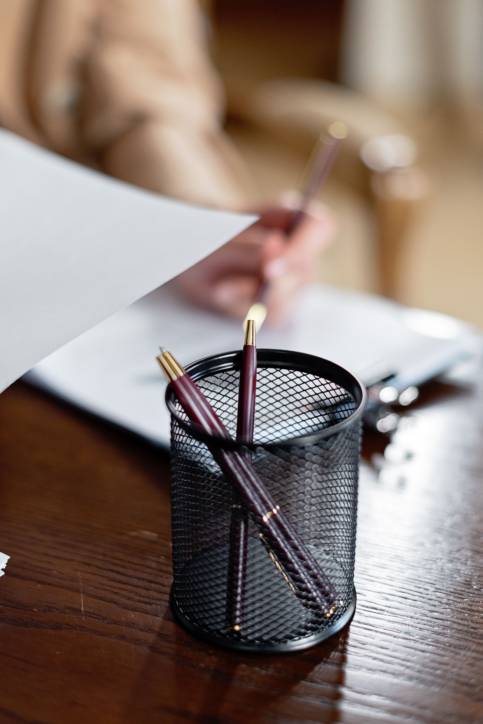 A hand holding paper beside a mesh pencil holder