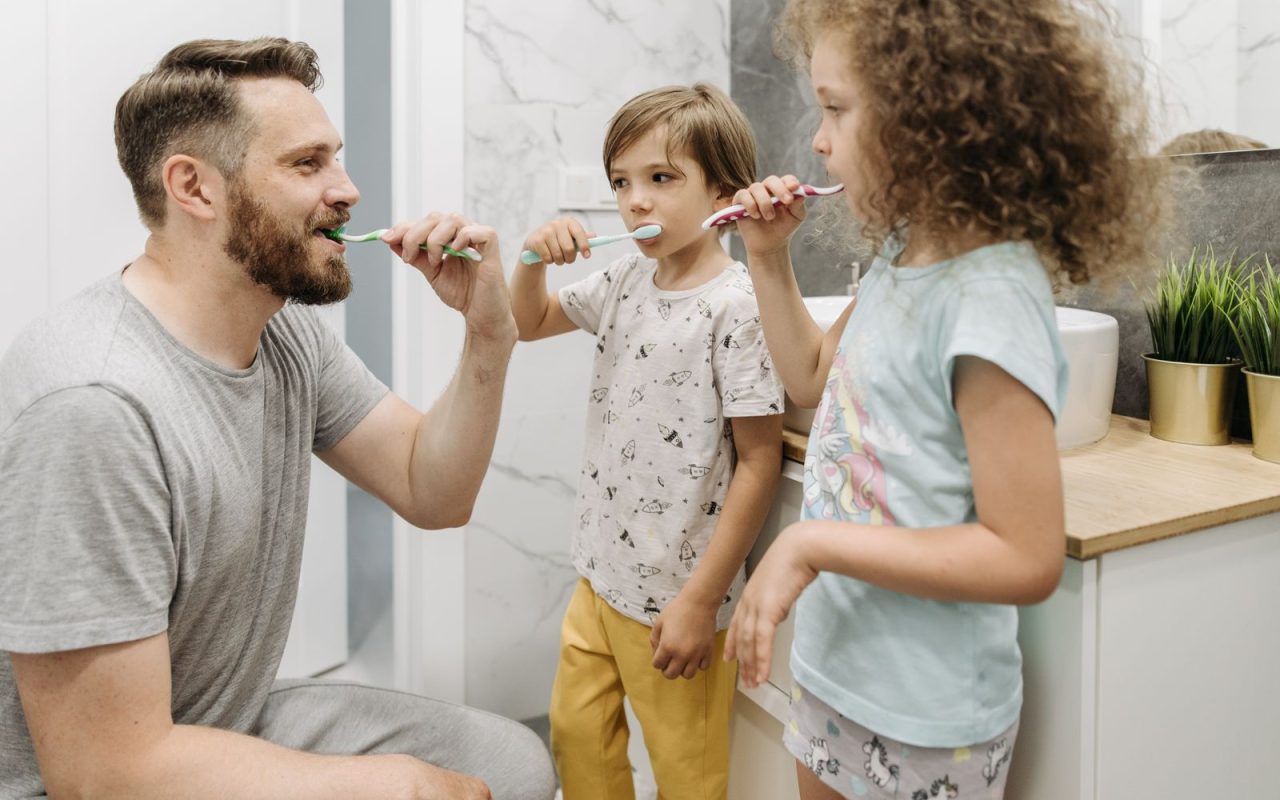 Father and two children brushing their teeth in a shared bathroom