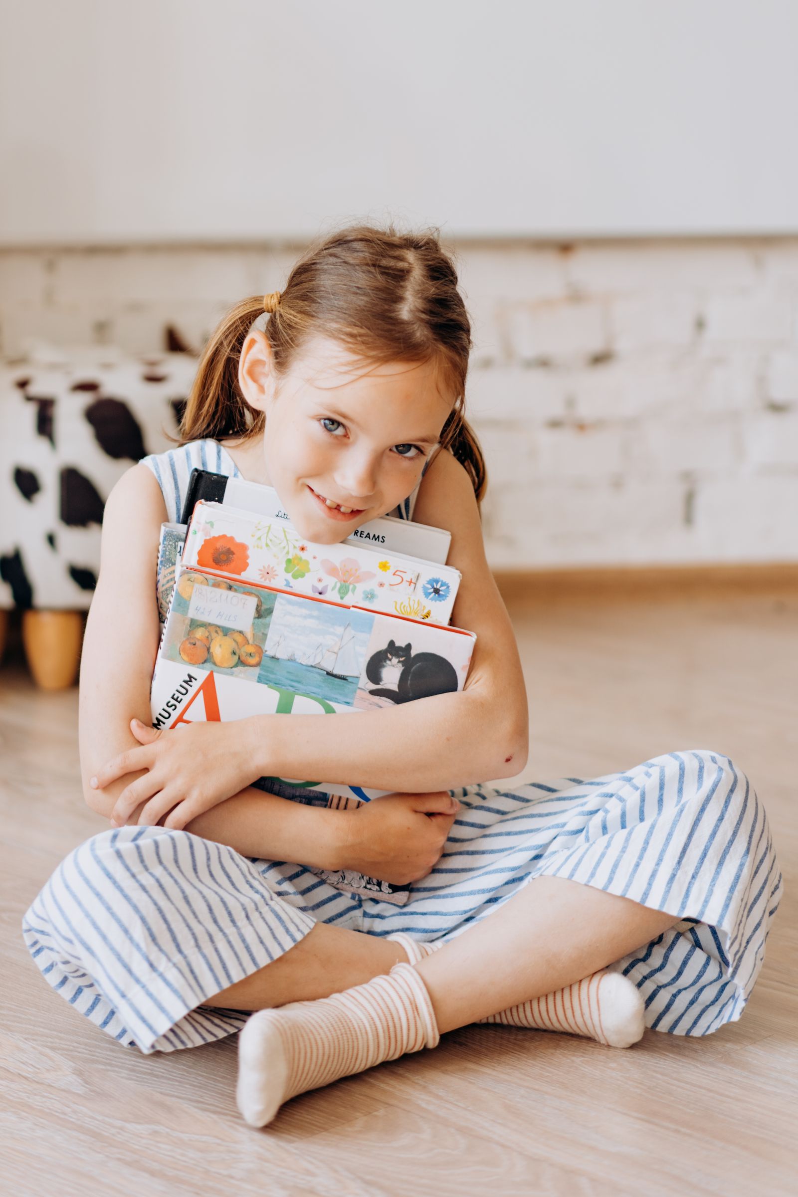 A young girl holding several picture books at home
