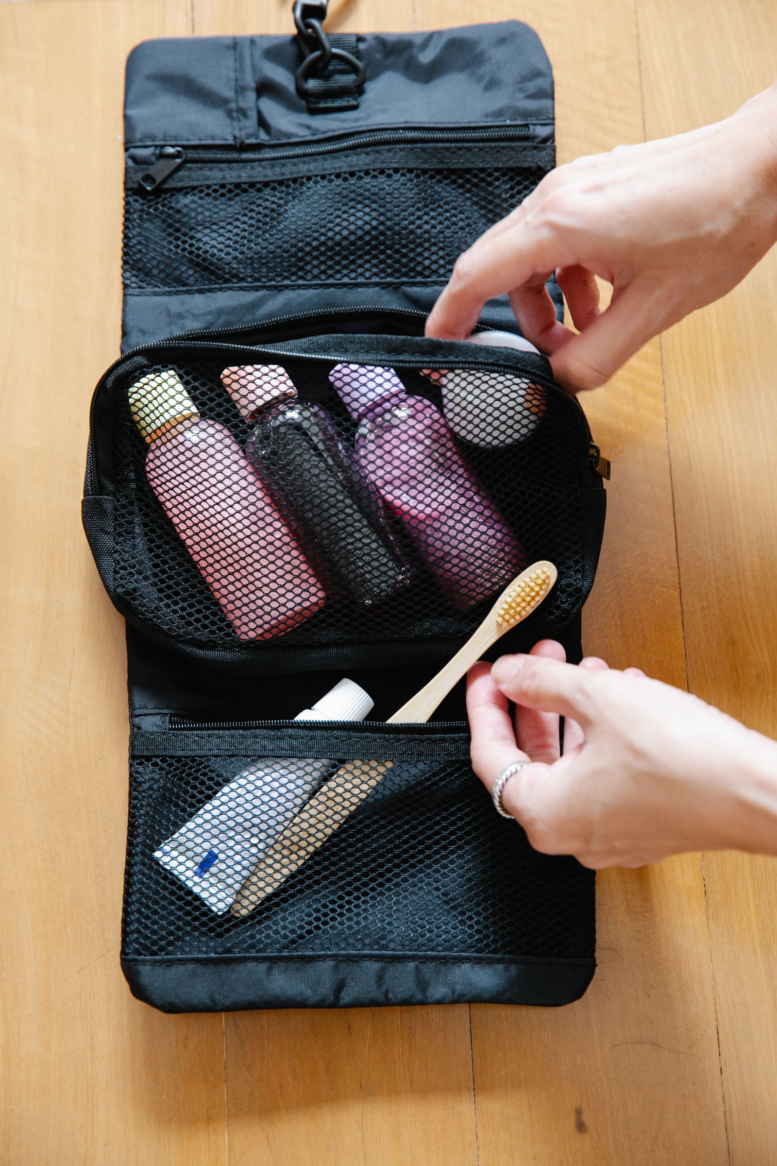 A hand packing a toothbrush and bottles into a toiletry bag