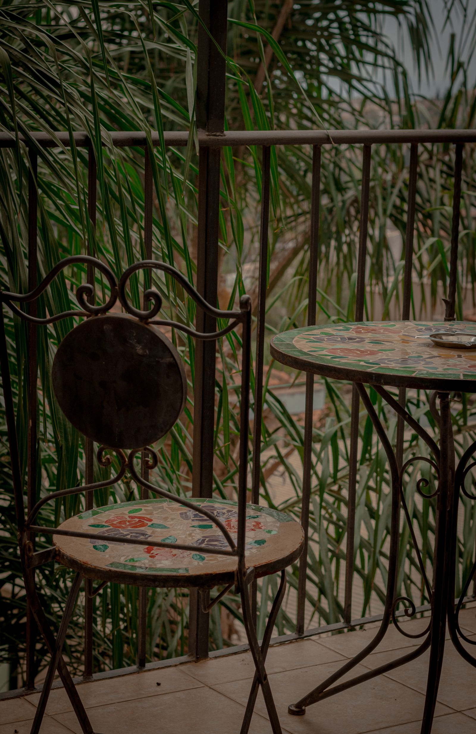 A vintage metal chair and table beside leafy balcony plants