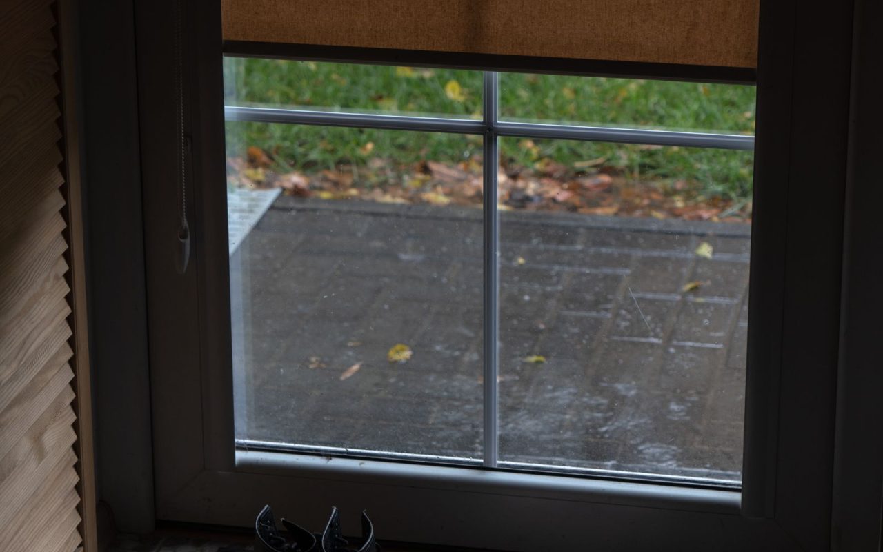 Shoes resting on a mat beside a rain-streaked doorway
