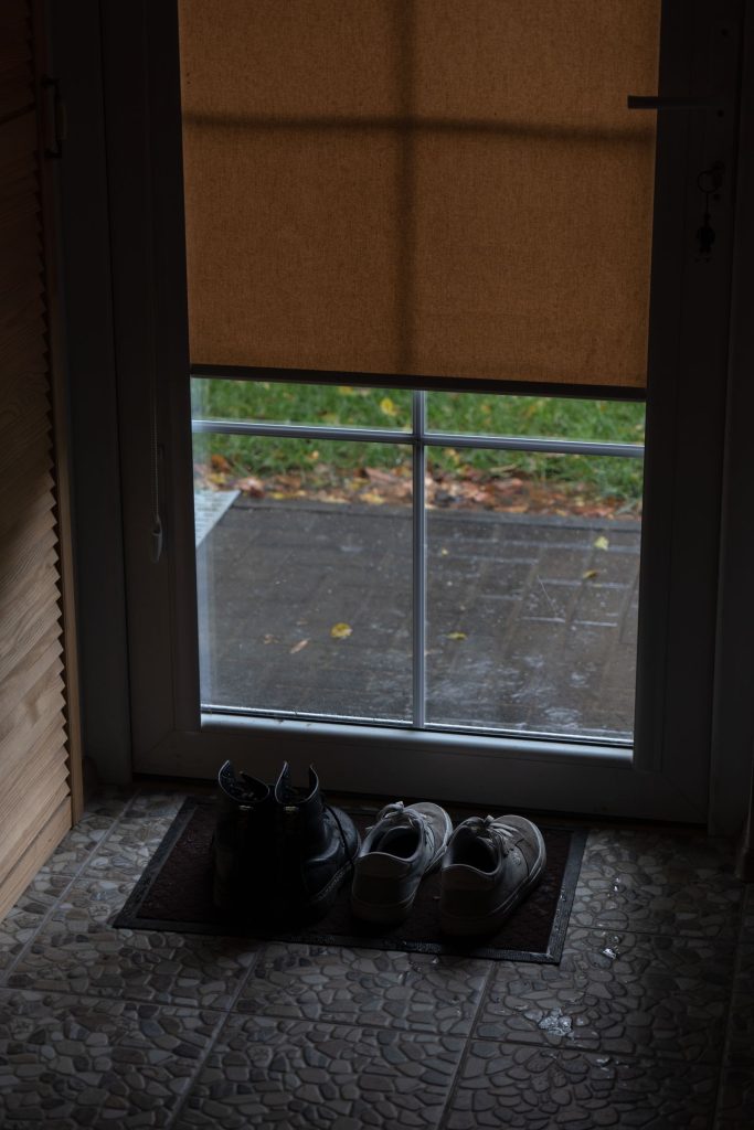 Shoes resting on a mat beside a rain-streaked doorway