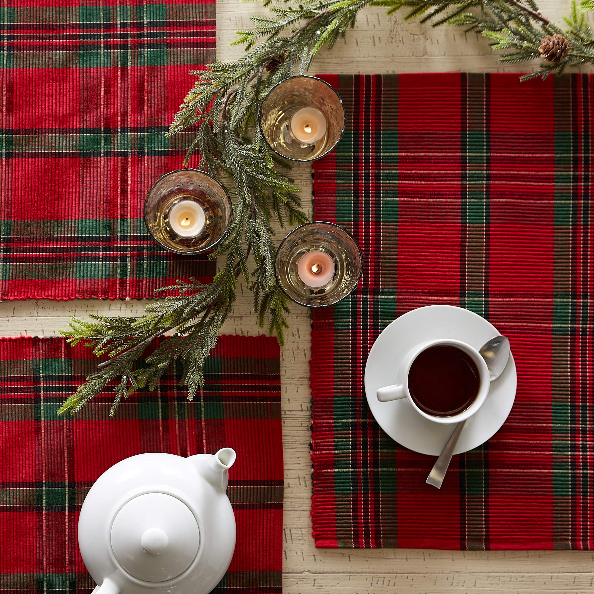 Two plaid DII holiday placemats on a table with separate cups and greenery