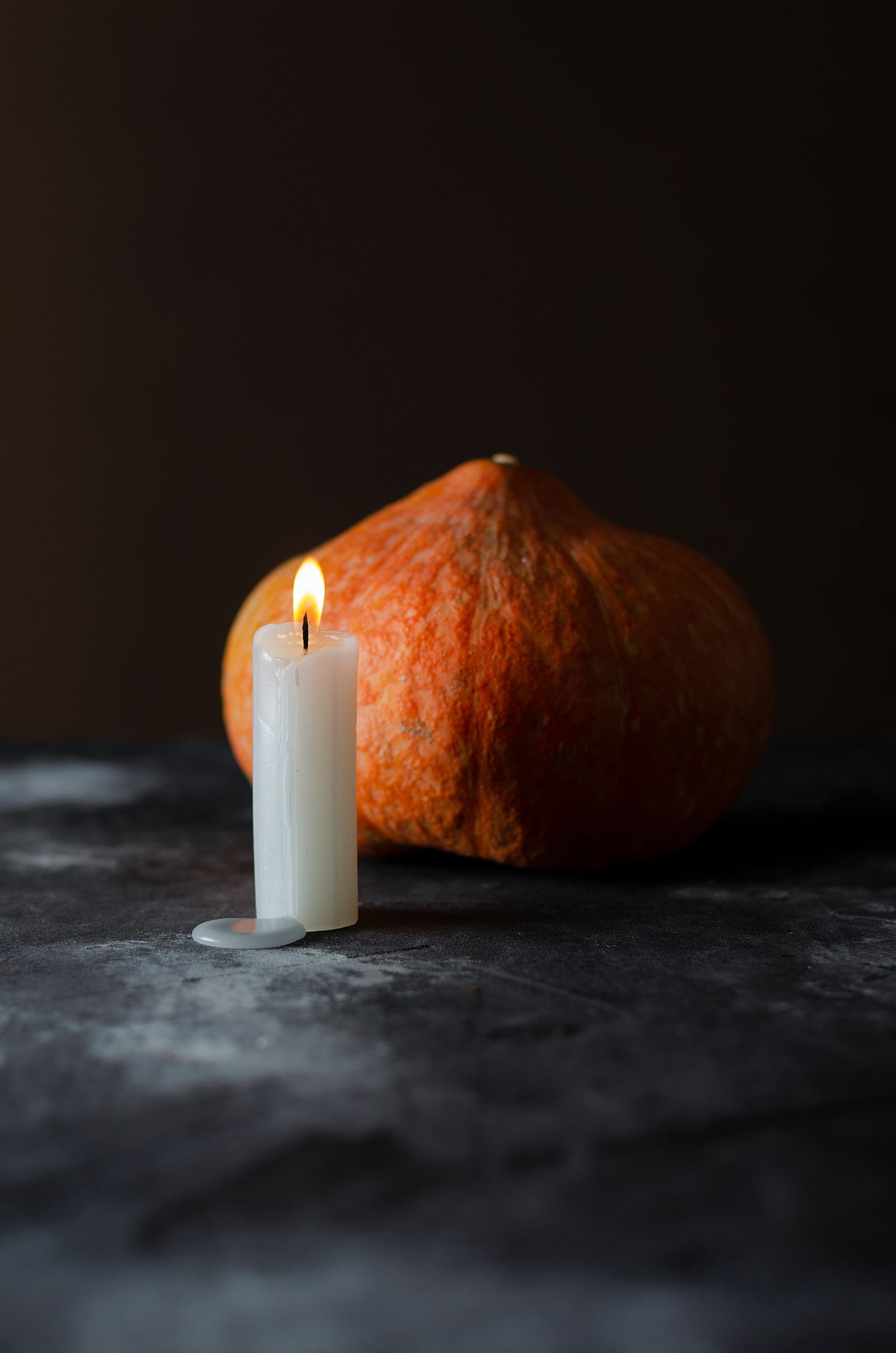A lit candle beside a pumpkin against a dark background