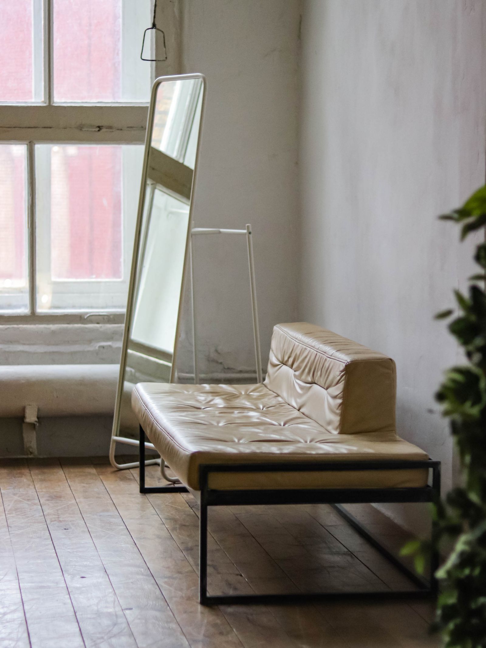A tall mirror beside a pale leather chair near a window